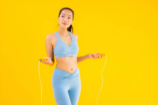 Güzel bir Asyalı kadın portresi. Sarı izole edilmiş arka planda egzersiz yapmak için iple spor giysisi giyiyor. - Fotoğraf, Görsel