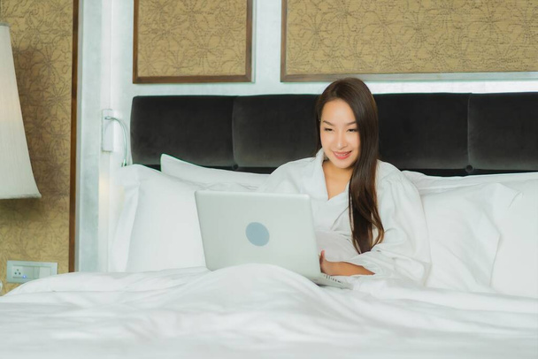 Portrét krásná mladá asijská žena použít počítač notebook na posteli v ložnici interiér - Fotografie, Obrázek