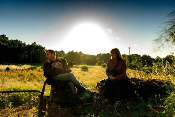 homme et femme assis sur un mur de pierre regardant quelque chose qui attire l'attention avec le soleil presque couchant - Photo, image