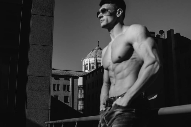 A young sexy athlete with perfect abs poses topless in jeans outside on a sunny day. Healthy lifestyle, proper nutrition, training programs and nutrition for weight loss. Black and white. - Foto, Bild