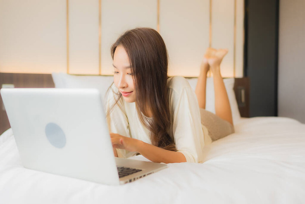 Portret mooie jonge aziatische vrouw gebruik laptop op bed in slaapkamer interieur - Foto, afbeelding