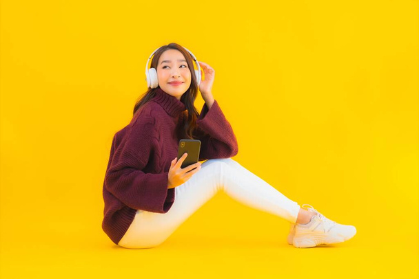 Portrait belle jeune femme asiatique utiliser téléphone portable intelligent écouter de la musique sur fond jaune isolé - Photo, image