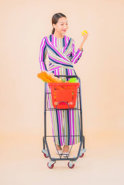 Portrait beautiful young asian woman with grocery basket from supermarket on color isolated background - Zdjęcie, obraz