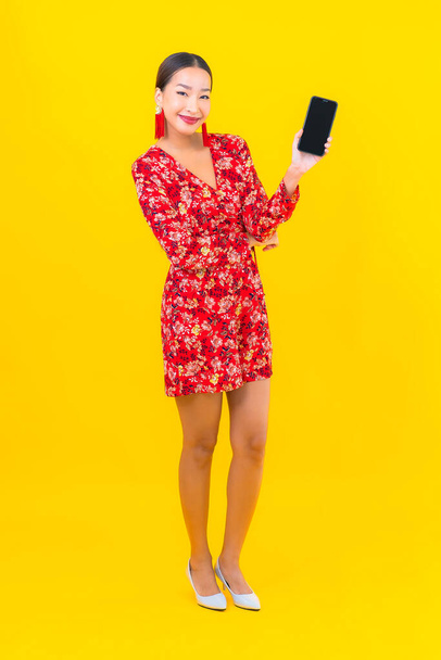 Portret mooie jonge aziatische vrouw gebruik slimme mobiele telefoon op gele kleur achtergrond - Foto, afbeelding