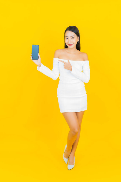 Портрет красивый молодой бизнес азиатской женщины со смартфоном на желтом фоне - Фото, изображение