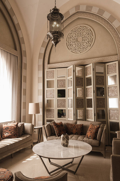 Wschodnia tradycyjna koncepcja projektowania wnętrz domowych. Orientalny salon z marmurowym stołem, sofą, poduszkami, okiennicą, dekoracjami - Zdjęcie, obraz