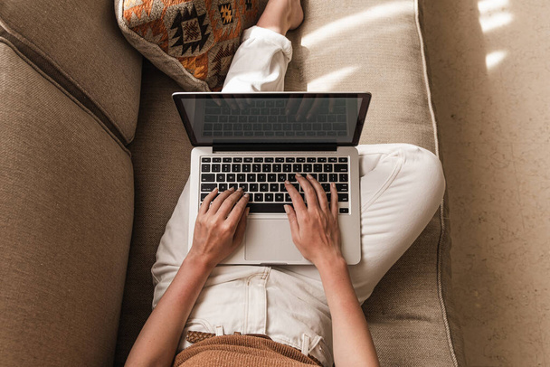 Young woman workin on laptop computer lying on the couch. Work at home at quarantine, freelancer concept. Girl boss - 写真・画像