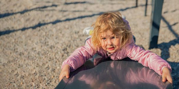 Una niña jugando en el patio sube la colina. Una actividad saludable de primavera u otoño para los niños. El niño juega alegremente al aire libre. - Foto, imagen