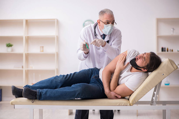 Giovane paziente di sesso maschile visita vecchio medico nel concetto di vaccinazione - Foto, immagini