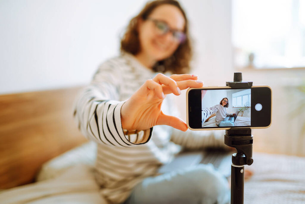 Young woman recording her video blog. Woman blogger videotapes her vlog at home. Vlogger makes online streaming using phone. Social media, instagram, stay home and quarantine. - 写真・画像