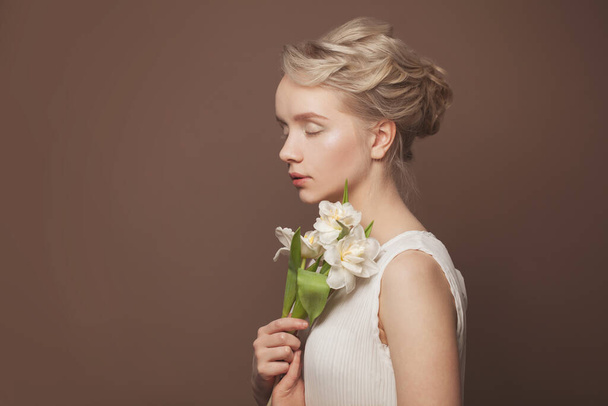 Beauty woman takes beautiful flowers in her hands on brown background - 写真・画像