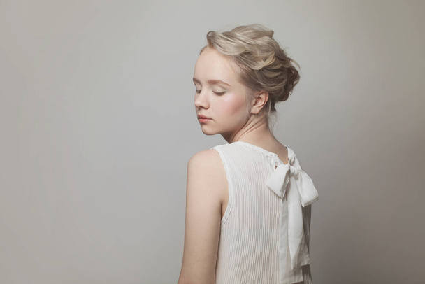 Perfect young blonde woman with gentle updo hair in white bow back blouse on white background - Valokuva, kuva