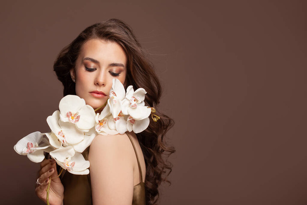 Attraktive brünette Frau Mode-Modell mit weißen schönen Blumen. Schöne weibliche Modell mit langen gesunden braunen Haaren auf braun - Foto, Bild