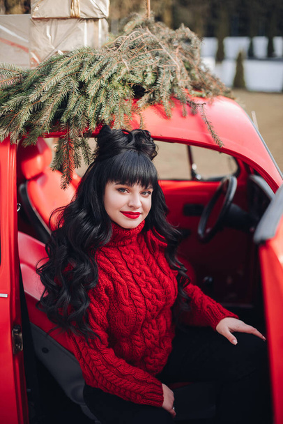 Young girl with dark hair sits in a beautiful red car in winter - Foto, Imagen
