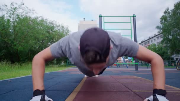 young guy performs push-up exercises on the street, a sports ground. by training the muscles of the arms and back. - Footage, Video
