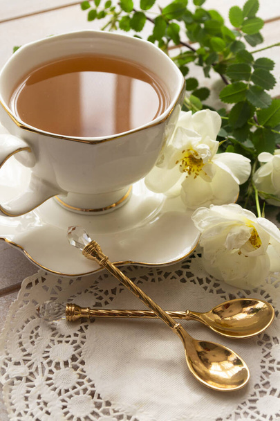 Magnífico ramo de rosas frescas en la antigua alusión antigua, cerámica, jarra de porcelana con oro en plato redondo envejecido, taza de té de china con cucharas de oro - Foto, imagen
