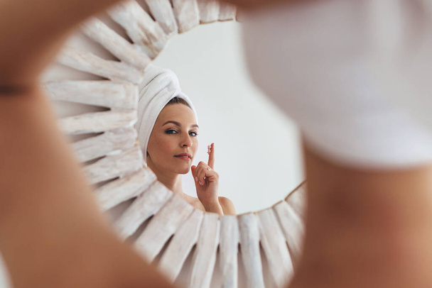 Женщина наносит крем на лицо, увлажняет кожу - Фото, изображение
