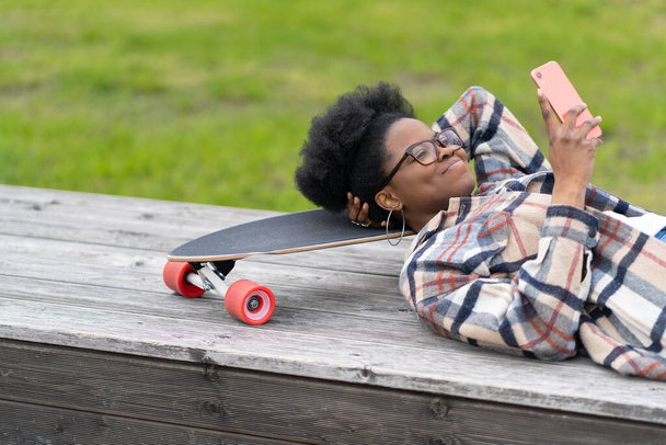 笑顔のスケーター女性は喜びの笑顔でスマートフォンで長いボードテキストや読み上げメッセージに横たわってリラックス - 写真・画像