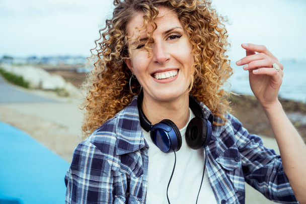 Close up Portrait of smiling curly hair caucasian woman with large headphones walking outdoor. Enjoy the moment and music. Freedom and happiness, simple pleasures concept. - Foto, Bild