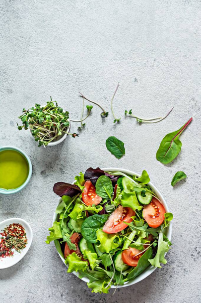 Friss saláta friss zöldségekkel, érett paradicsommal, uborkával, salátával és mikrozölddel, szürke alapon tálban. Egészséges nyers étel koncepció. A szöveg helye, a másolási hely. - Fotó, kép