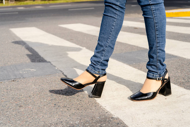 Woman's legs with shoes and pants crossing a street on the pedestrian path or zebra crossing. Road safety concept. - Photo, image