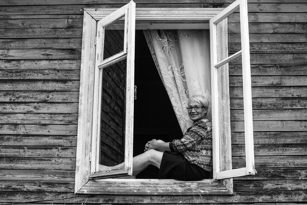 An adult woman sitting on the window of a village house. Black and white photo. - Foto, Imagem