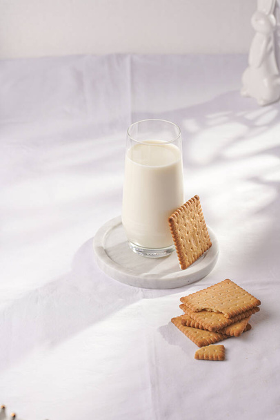 A glass of milk on a marble plate on a white table cloth and freshly baked cookies - Fotó, kép