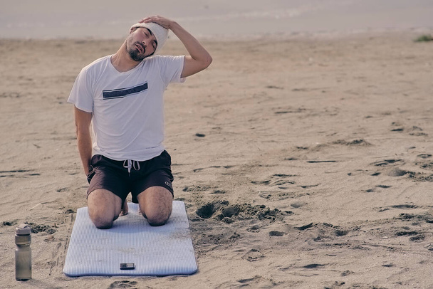 Yoga yaparken, pozisyonlar ve esneme hareketleri yaparken plajda dinlenen genç çocuk. - Fotoğraf, Görsel