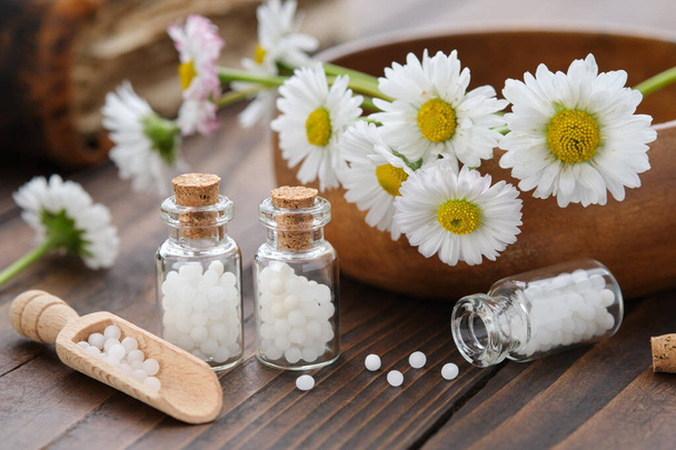Bottles of homeopathy granules. Homeopathic remedy - Chamomilla. Daisies flowers in wooden bowl. Homeopathy medicine concept.  - Фото, зображення