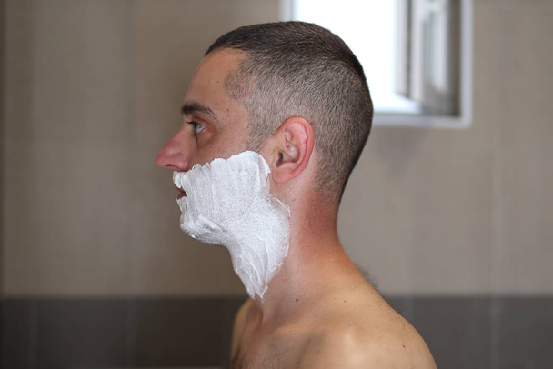 A férfi a fürdőszobában borotvahabbal az arcán borotválkozásra kész. Férfi szépség koncepció. Zárás és másolás - Fotó, kép