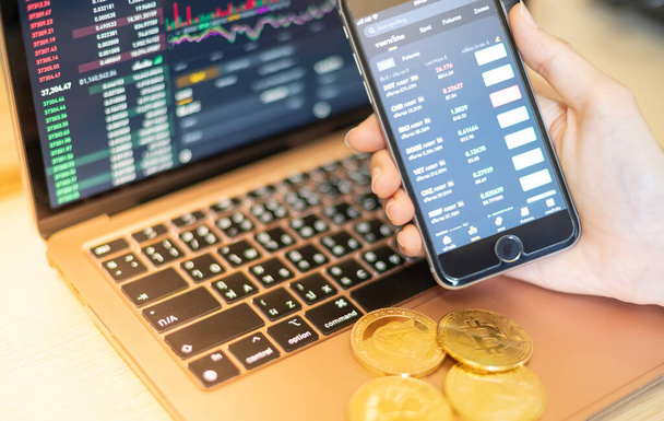 The business holding the smartphone for investors trading with the cryptocurrency coin on the laptop with a display screen and pointing to the data presented and deal on a stock exchange. - Foto, imagen