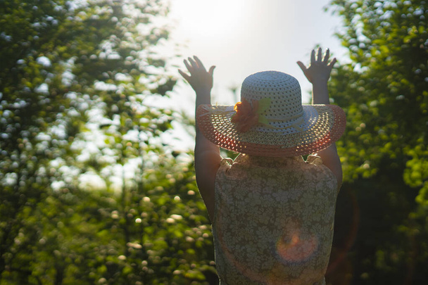 widok z tyłu dorosła kobieta w letniej czapce podnieść ręce do słońca - Zdjęcie, obraz
