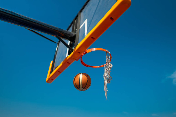 Balón de baloncesto cayendo a través de la vieja red. Cielo azul sobre fondo - Foto, Imagen