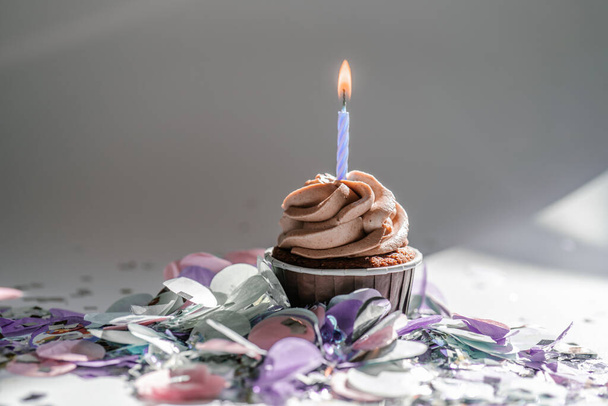 A cupcake with a candle stands on a white background with a shadow. - Photo, image