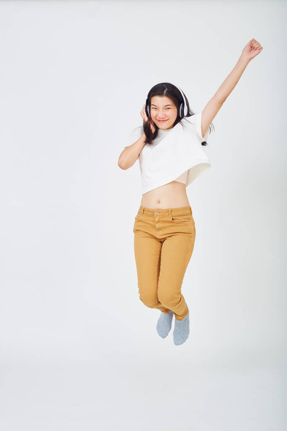 ヘッドフォンを持つ若いアジアの女性と色の背景にジャンプ - 写真・画像