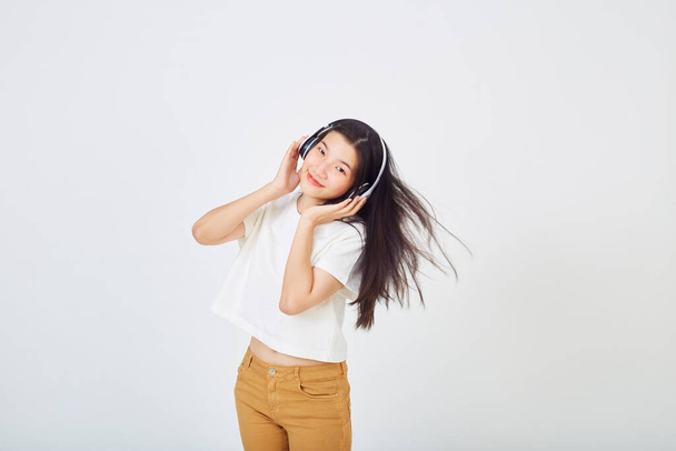 Jovem mulher asiática com fones de ouvido e dançando em fundo branco - Foto, Imagem
