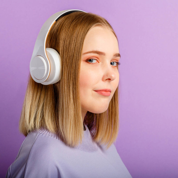 Confident Young woman in headphones portrait. Beautiful serious woman with blonde hairstyle enjoy listen song music in headphone isolated over purple color background. Closeup square - Fotografie, Obrázek