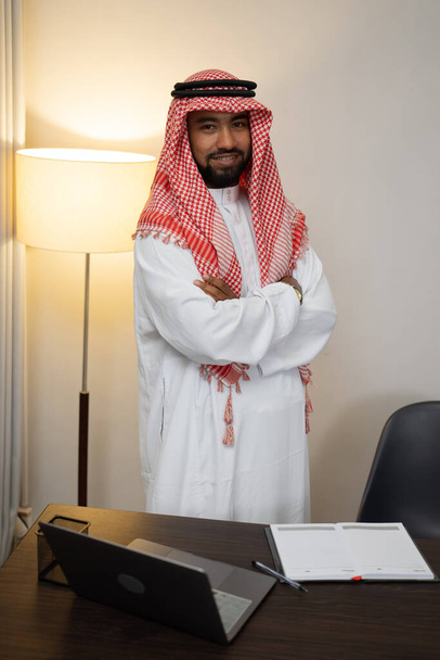 een Arabische zakenman met gekruiste handen staat achter een laptoptafel - Foto, afbeelding