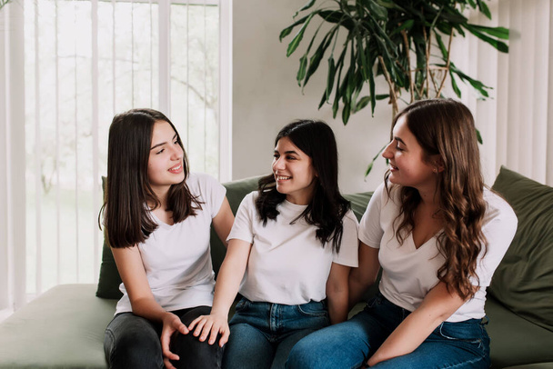 Τρία όμορφα χαμογελαστά καυκάσια κορίτσια με λευκό πουκάμισο κάθονται στον πράσινο καναπέ. Φίλοι που μιλούν συναισθηματικά και συζητούν τα τελευταία νέα και τη ζωή, μοιράζονται τις σκέψεις τους και έχουν κάποια κουτσομπολιά - Φωτογραφία, εικόνα