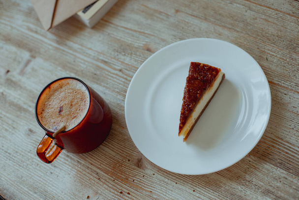 Coffee in a glass cup and nutty cheesecake on a white plate stand on a wooden table. - Fotoğraf, Görsel