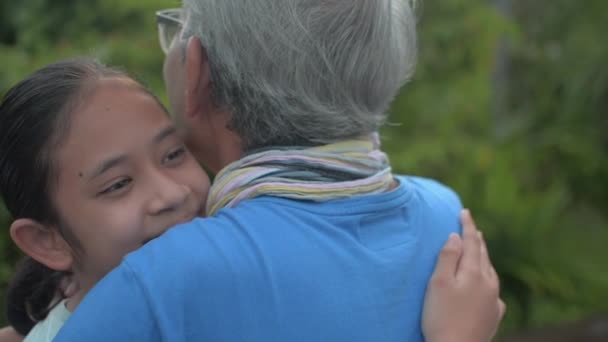 Mutlu Asyalı sevimli torun bahçede dikilirken gri saçlarına sarılıyor. Yaşlı büyükbabayı sevgiyle kucaklamak. Birliktelik. İki nesilde kaynaşma. - Video, Çekim