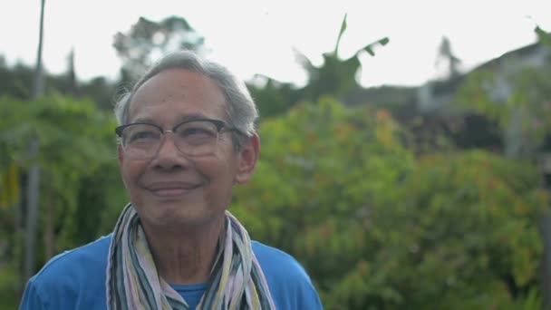 Gözlüklü mutlu Asyalı büyükbaba ön bahçede dururken torununa sarılıyor. Gülümseyen gri saçlı yaşlı adam torununu kucaklıyor ve kafasını okşuyor. Aşkın ifadesi. Kırsal alan. - Video, Çekim