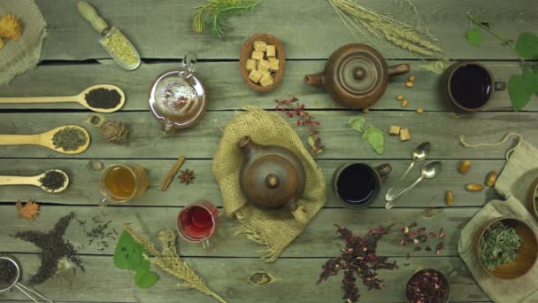古い木製のテーブルの上にお茶。平置きだ。紅茶の異なるタイプのまだ生活:黒、緑、仲間、ハイビスカス、花、果物、ハーブ。 2人の男性と1人の女性の手はそれぞれお茶のカップを取ります(緑、ハイビスカス、黒)). - 映像、動画