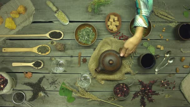 Red tea made from rose petals on an old wooden table. Flat lay. Still life with different types of tea: black, green, mate, hibiscus, floral, fruit, herbal. A man's hand pours hibiscus tea into mugs. The hands of a man and a woman take these mugs. - Footage, Video