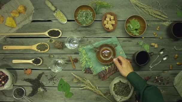 Green tea on an old wooden table. Flat lay. Still life with different types of tea: black, green, mate, hibiscus, floral, fruit, herbal.A man's hand pours green tea into mugs. The hands of a man and a woman take these mugs. - Footage, Video