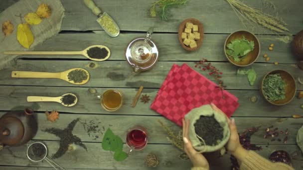 古い木製のテーブルの上に紅茶。平置きだ。紅茶の異なるタイプのまだ生活:黒、緑、仲間、ハイビスカス、花、果物、ハーブ。女性の手はテーブルの上に黒茶の袋を置きます。スローモーション2. - 映像、動画