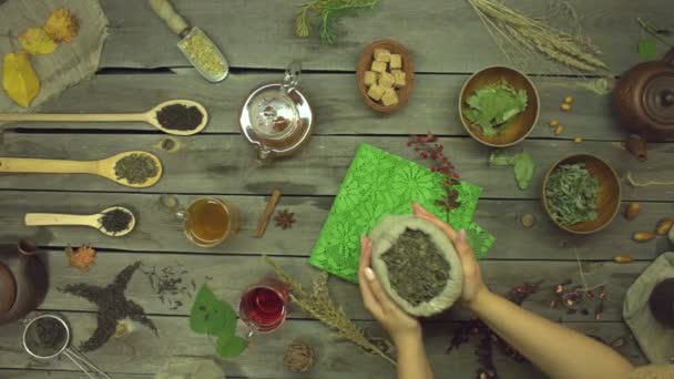 Green tea on an old wooden table. Flat lay. Still life with different types of tea: black, green, mate, hibiscus, floral, fruit, herbal.Women's hands put a bag of green tea on the table. Slow motion 2x. - Footage, Video