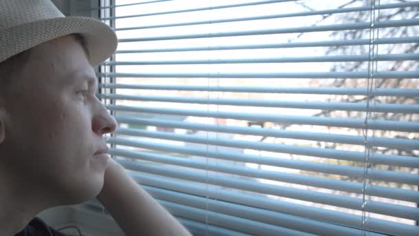 Een man met een hoed zit bij het raam, drinkt wat en kijkt met belangstelling naar wat er op straat gebeurt. - Video