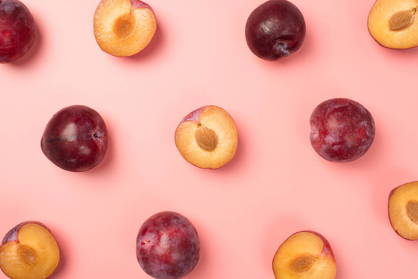 Top view photo of halves and whole plums on isolated pastel pink background - Zdjęcie, obraz