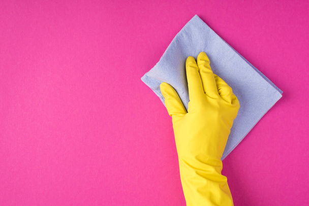 Bovenaanzicht foto van hand in hand in gele handschoen met blauwe viscose doek op geïsoleerde roze achtergrond met copyspace - Foto, afbeelding